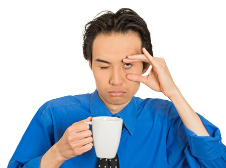 Man drinking coffee and holding his eye open from fatigue